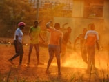 Local children playing football on a dusty field under a bright sky.