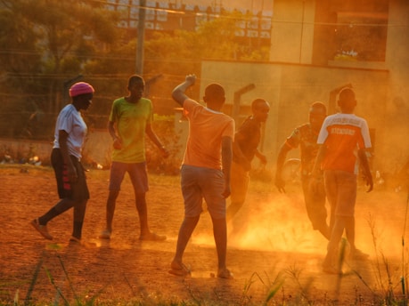 Children playing football on a dusty field during a local sports event.