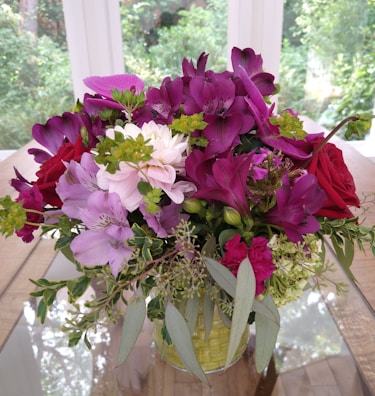 A vibrant bouquet of mixed flowers in a rustic vase on a wooden table.