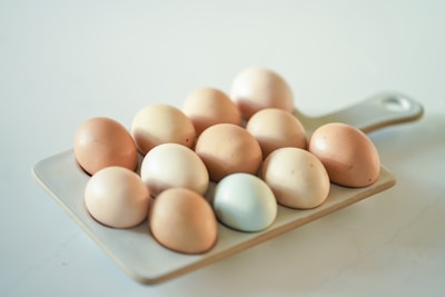 A collection of eggs of various colors, including brown, beige, and pale blue, are neatly arranged on a rectangular cutting board. The scene is set against a soft, light background, creating a gentle and serene appearance.
