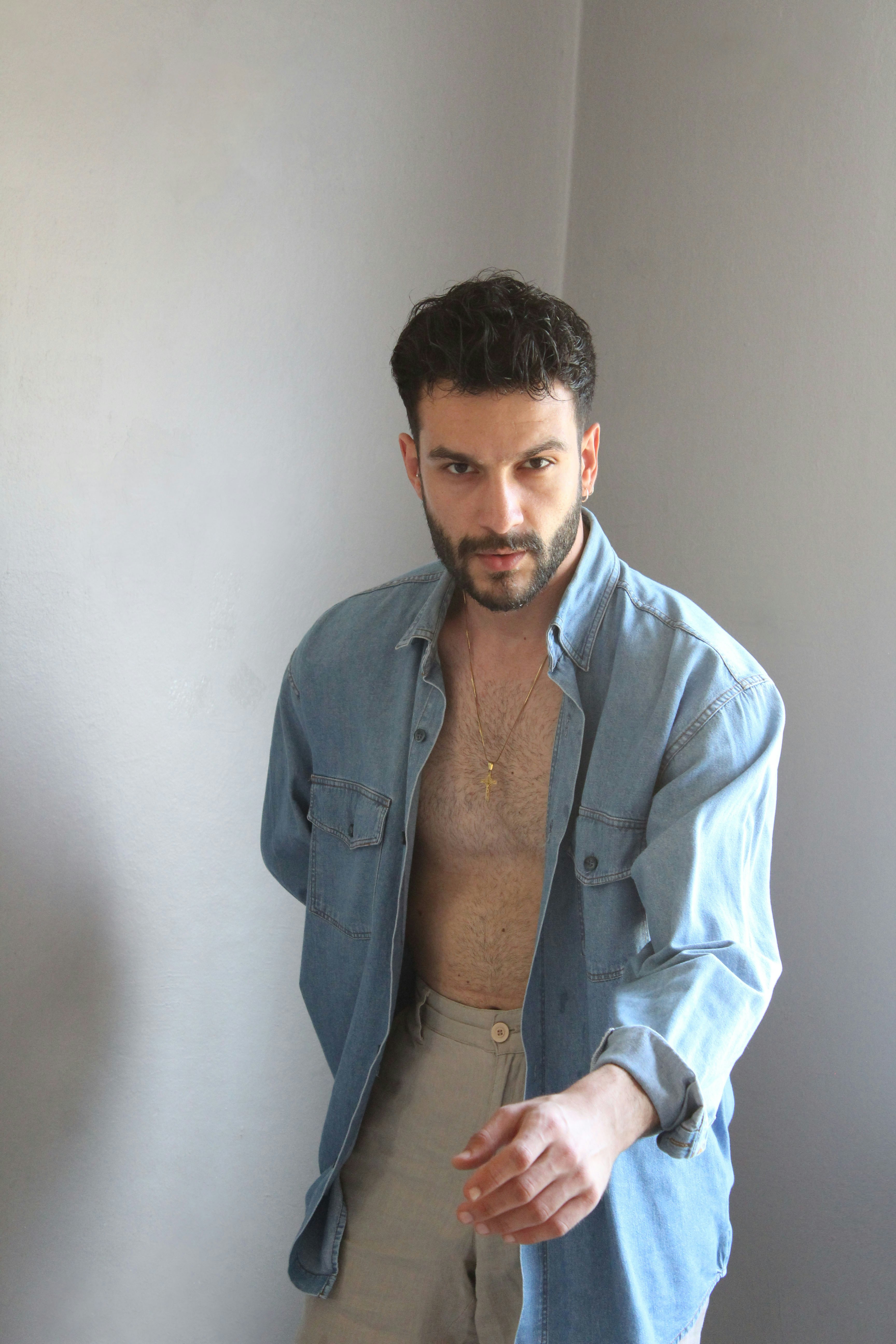 Relaxed man with 5-day stubble beard, casual setting, warm ambient light, confident relaxed expression against dark textured wall