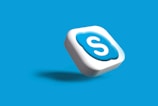 A 3D icon with the letter 'S' in white, encased in a blue cloud-like shape on a white square. It appears to be floating with a shadow cast below it, set against a solid blue background.