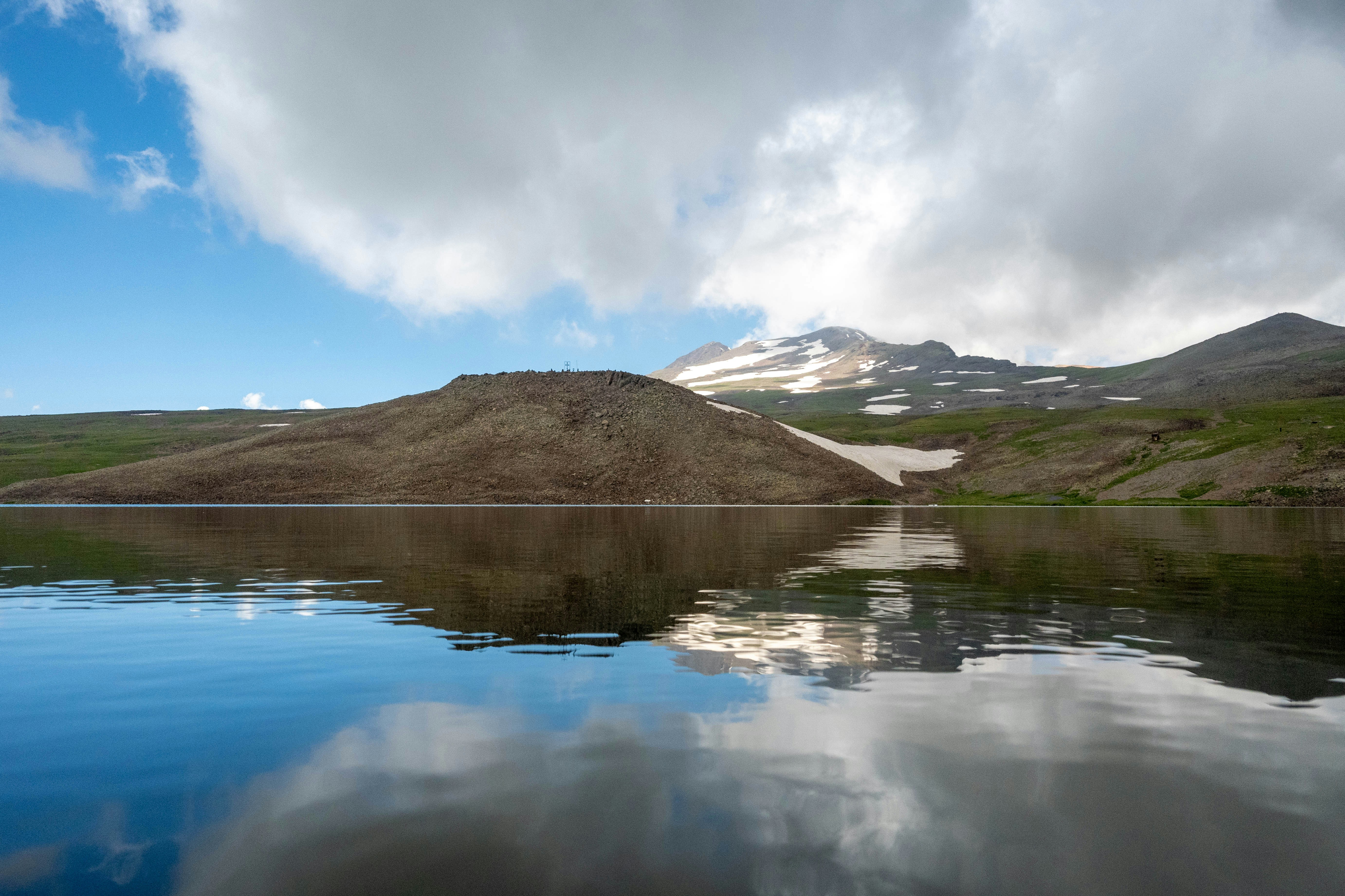 a body of water with hills in the background, Mount Aragats is reflected in the waters of Lake Kari.