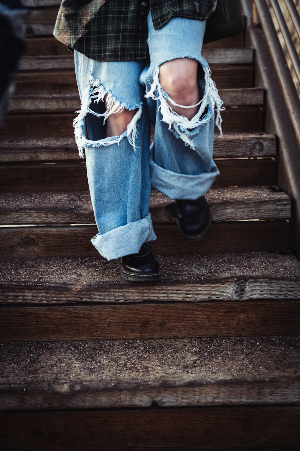 a person's legs in jeans and a blue shirt on a wooden staircase