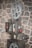 A vintage film projector is positioned against a rough stone wall. The device features large metal spools and intricate mechanical components with dials and buttons, suggesting a classic design from an earlier era of cinema.