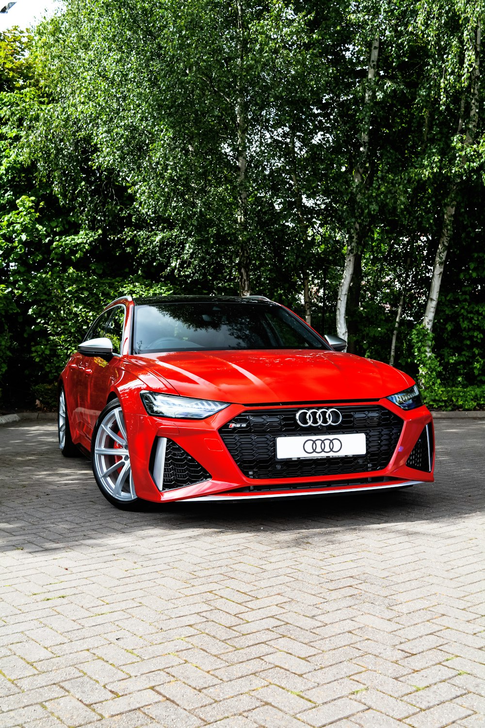 a red sports car parked on a brick road with trees in the background