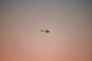 A sleek helicopter flying low over lush green backwaters at sunset.