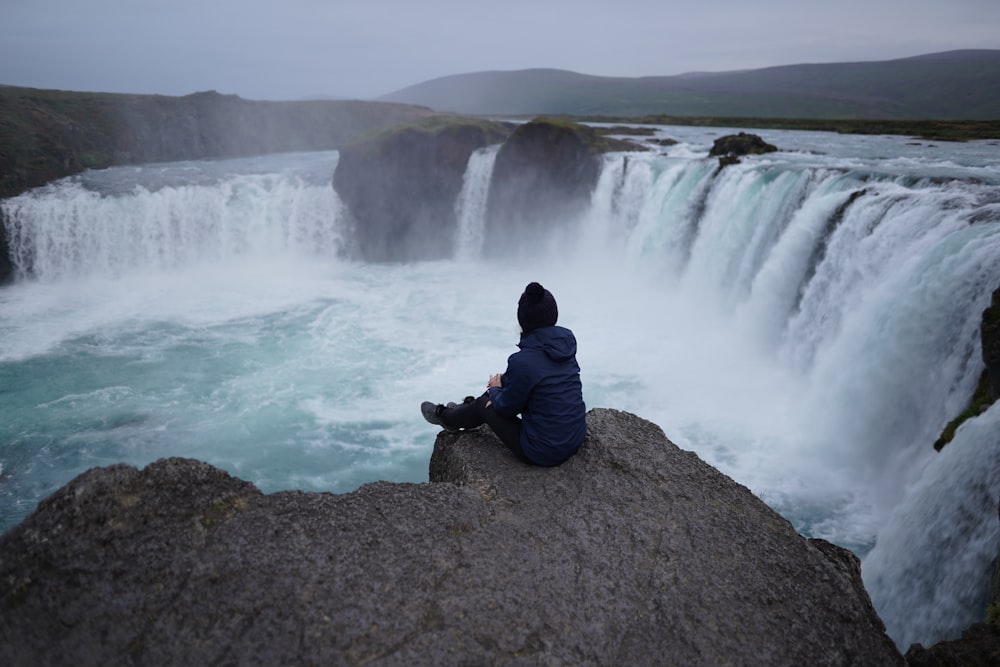 a person sitting on a rock looking at a waterfall