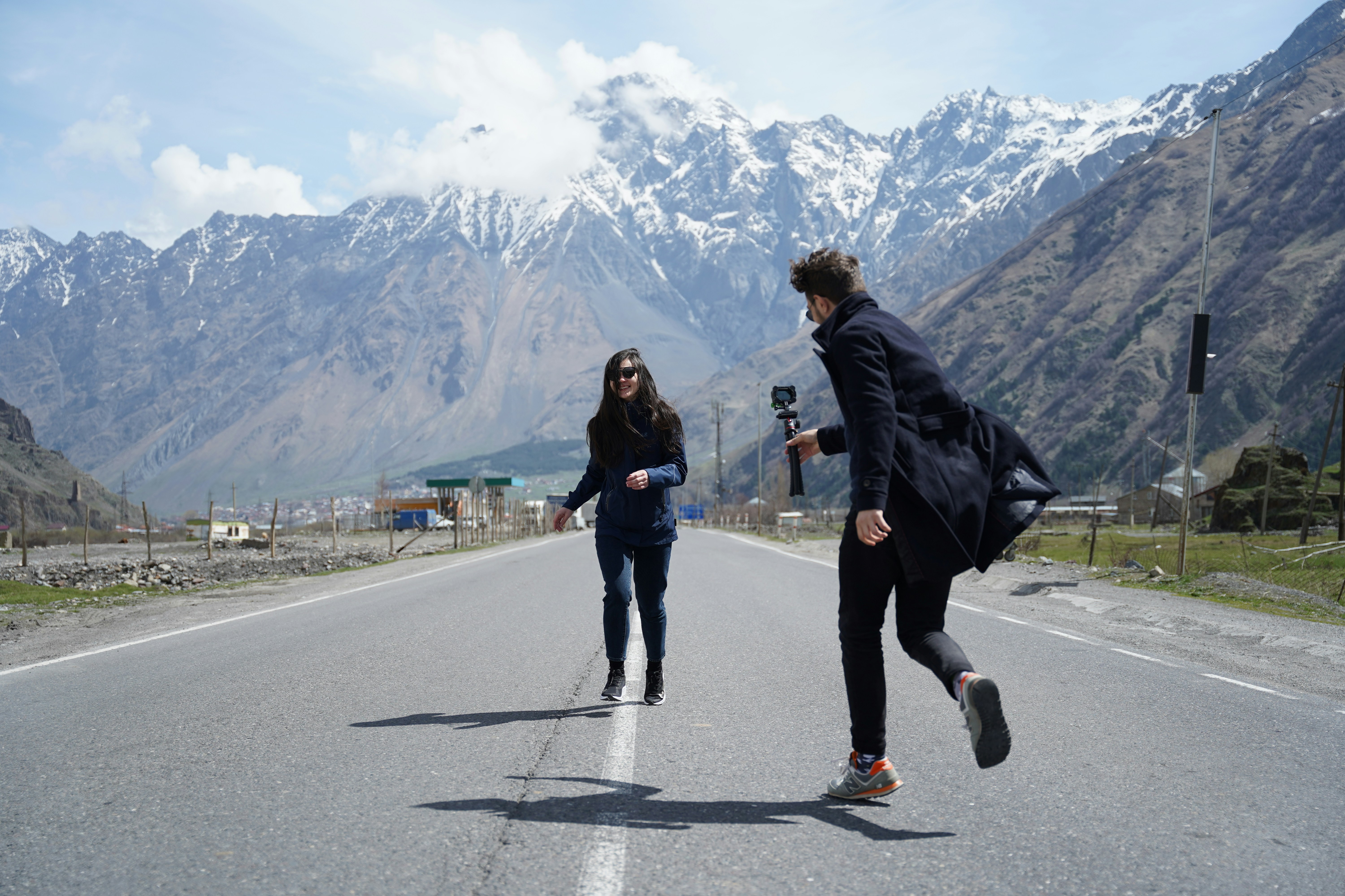 a man and woman running on a road with mountains in the background