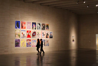 a man and woman standing in a room with a wall of paintings