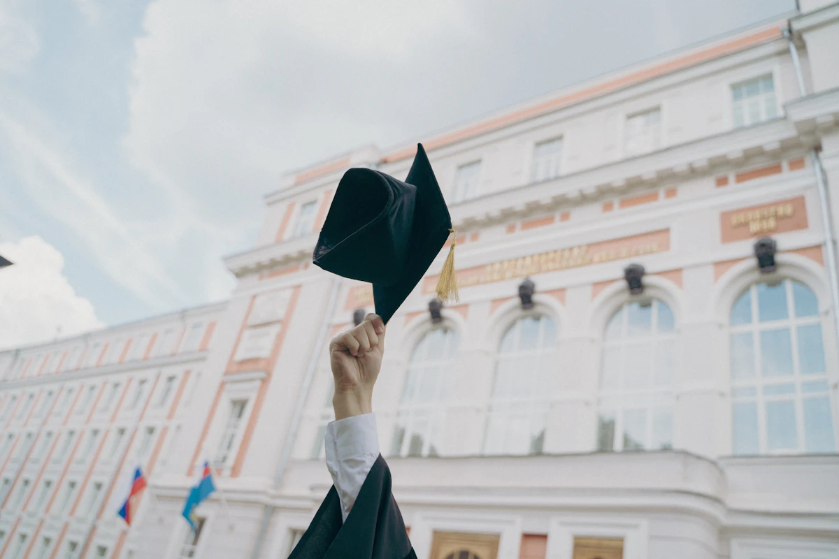 Graduation cap held up in front of a university building