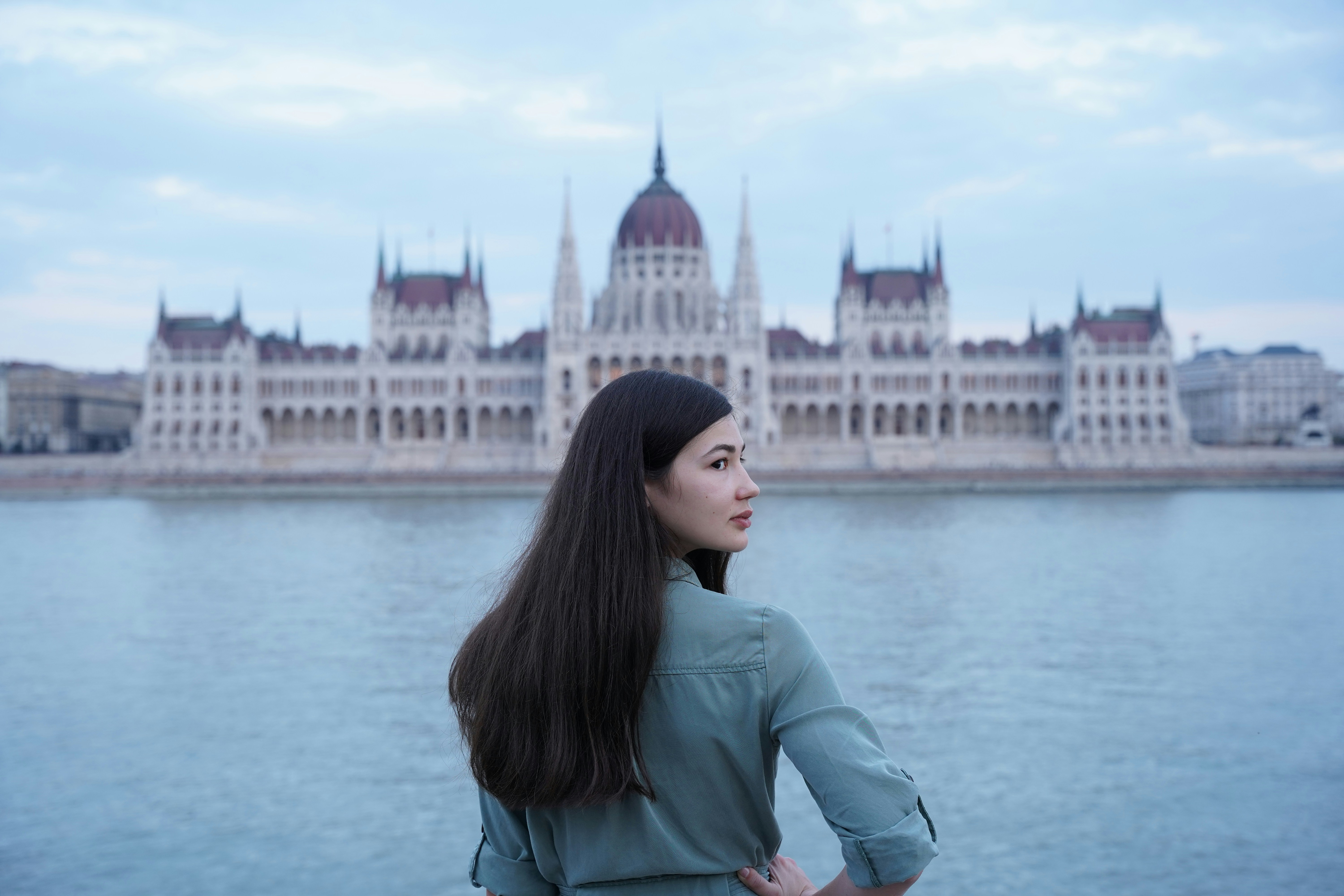 a man posing in front of a body of water with a large building in the background