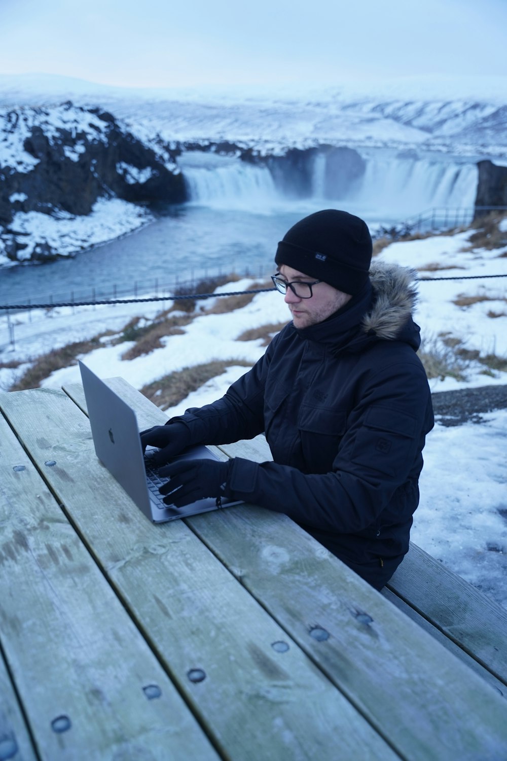 Eine Person sitzt auf einer Bank mit einem Laptop im Schnee