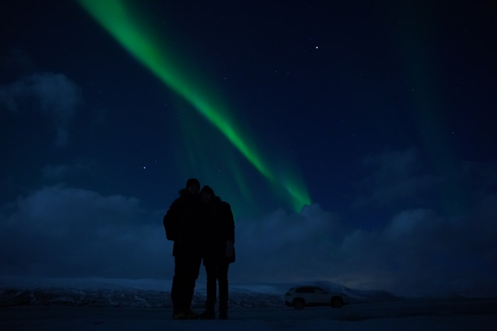 a group of people looking at a green aurora in the sky