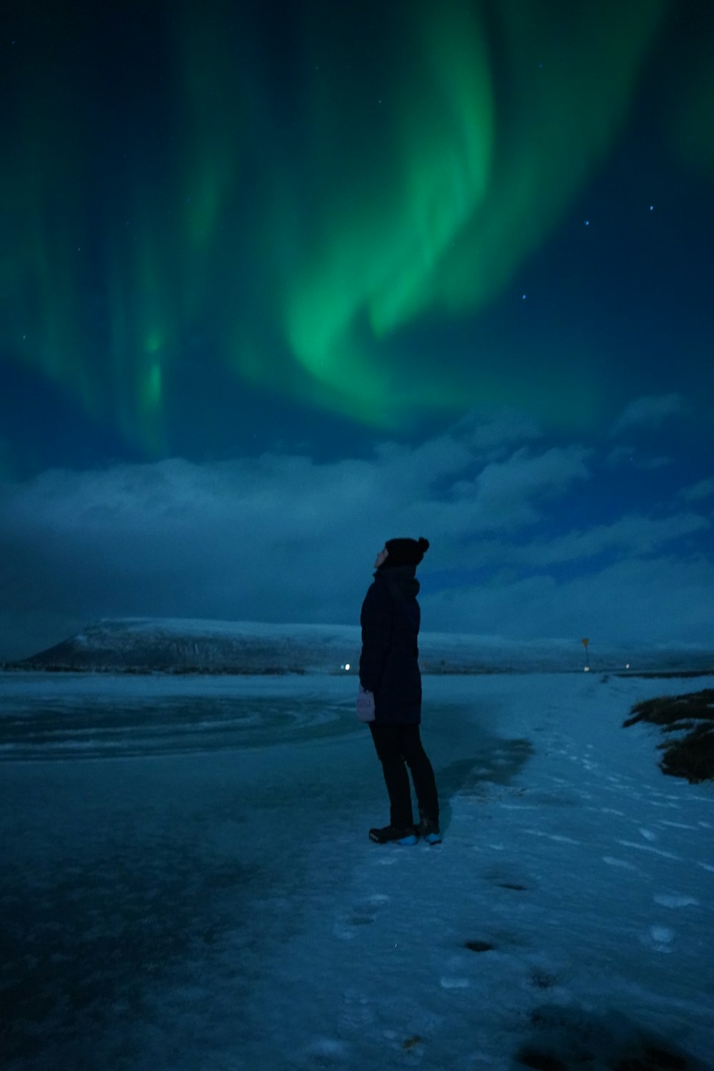 Una persona in piedi nella neve con un'aurora verde sullo sfondo