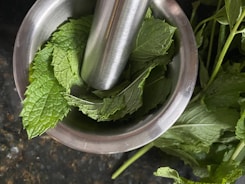 Fresh mint leaves and a small bowl of clear mentha oil on a wooden surface