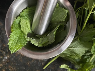 Fresh green leaves and flowers laid out beside a wooden mortar and pestle.