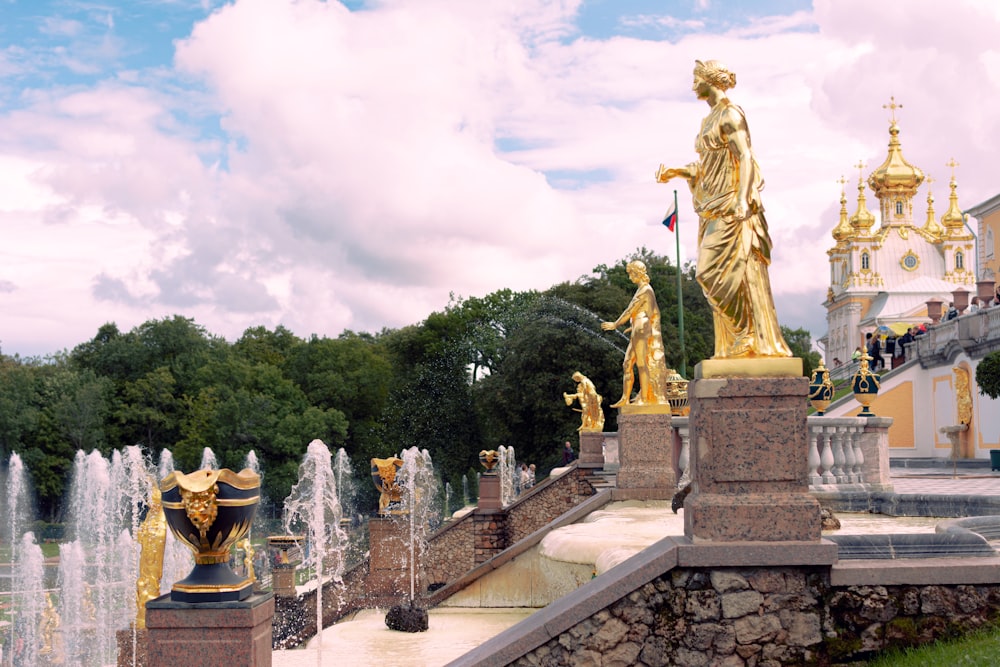 a group of statues on a stone wall with trees and a building in the background