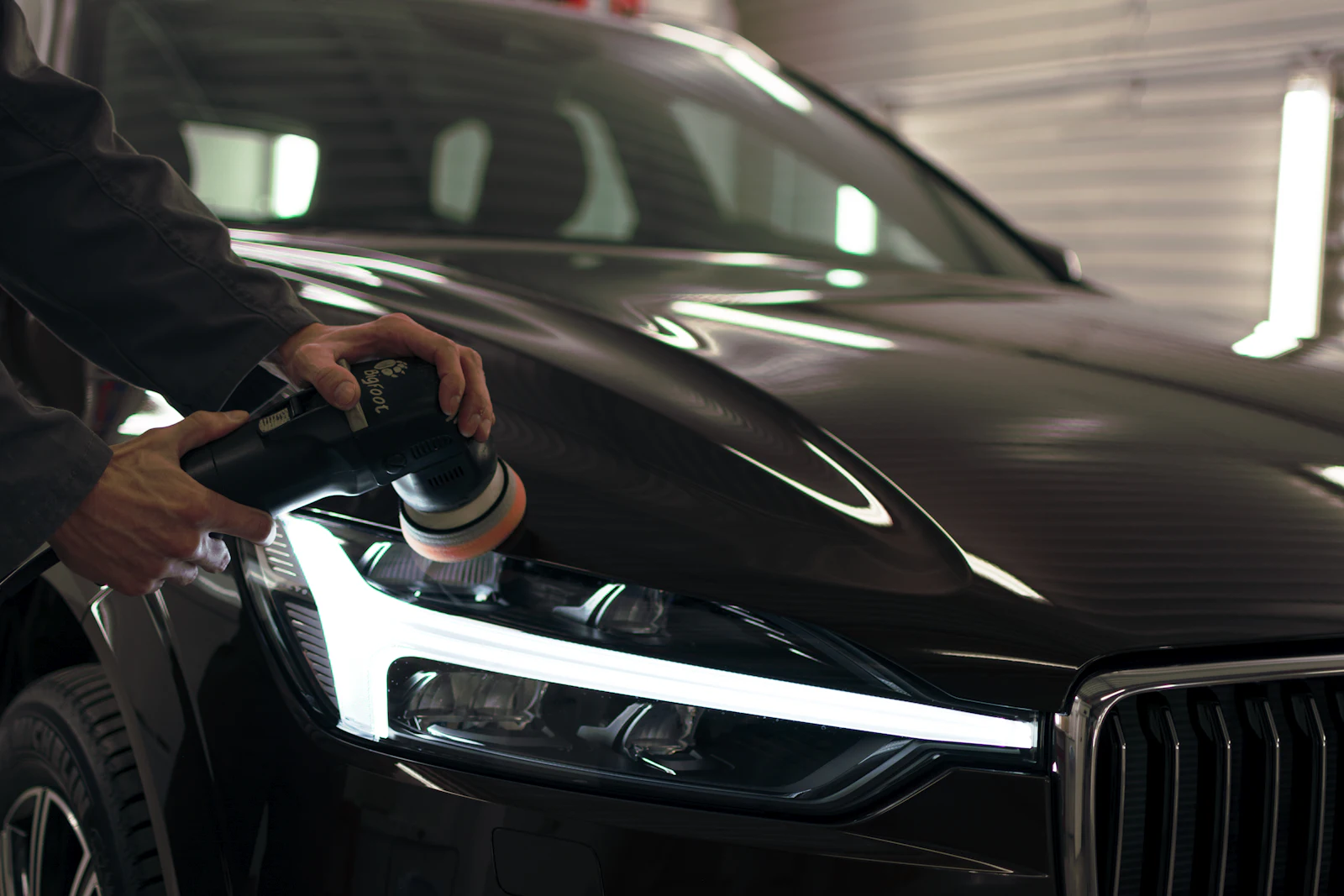 A detailer machine-polishing the hood and headlight of a black SUV