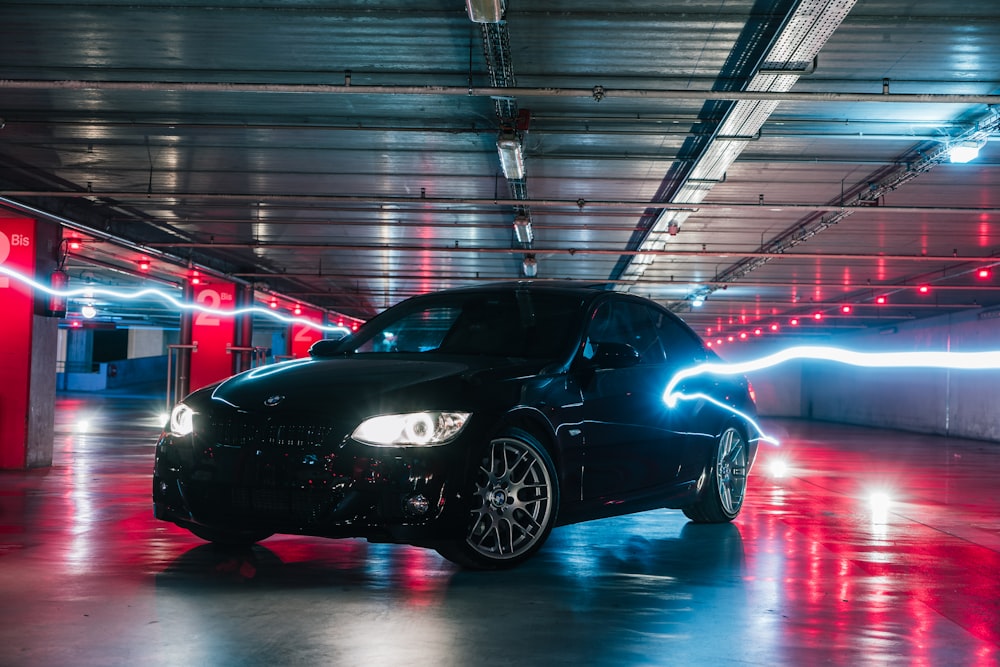 um carro preto estacionado em uma grande sala com luzes vermelhas