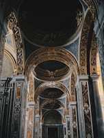 An intricately decorated interior with ornate arches and golden embellishments. The design features detailed carvings and symmetrical patterns, enhancing the grandeur of the space. The lighting appears soft, creating a serene and majestic atmosphere.