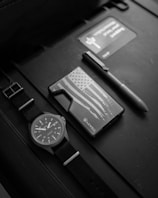 A MontLee watch placed on a stone surface alongside a walnut brown leather wallet and a minimalist notebook.