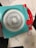A geometric drawing tool with a turquoise frame and red handles used to create intricate spiral patterns. Several examples of the patterns, in various colors, are seen on white sheets underneath the tool.