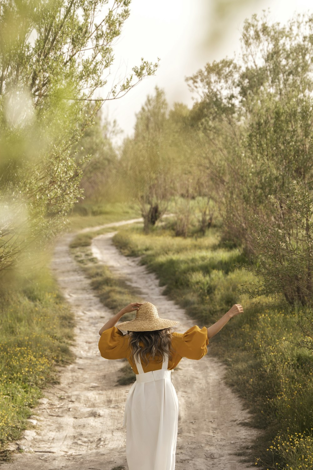 a person in a white dress and hat walking on a dirt path
