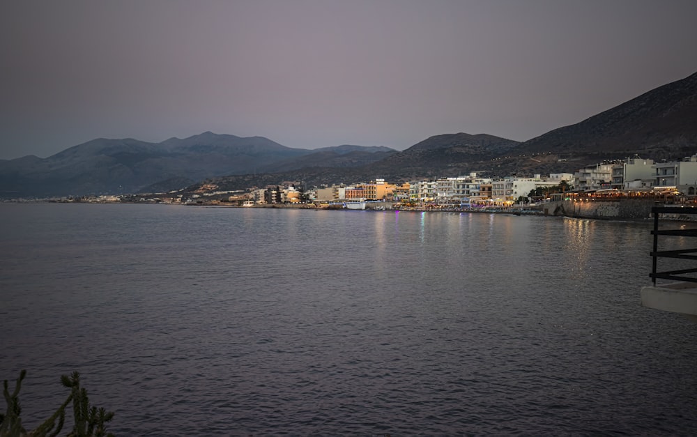 a body of water with buildings and mountains in the background