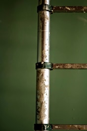 A close-up of a metal ladder against a green background with visible paint peeling and a worn, aged texture on its surface.