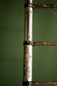 A close-up of a metal ladder against a green background with visible paint peeling and a worn, aged texture on its surface.