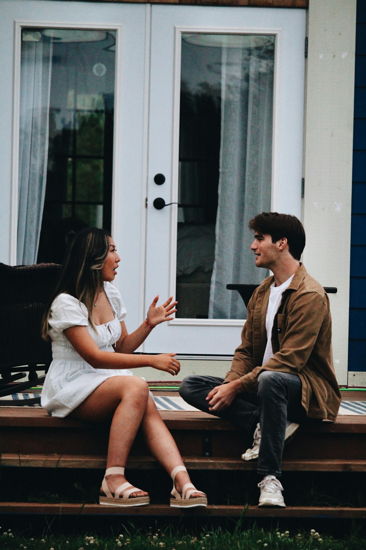 Two people in unhurried conversation on a porch, attentive-listening register