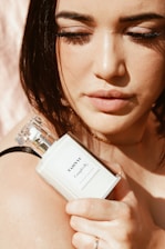 A close-up of a stylish woman applying perfume with a soft smile, bathed in warm natural light.