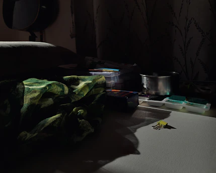 A dimly lit studio with scattered art supplies and soft shadows creating an intimate atmosphere.