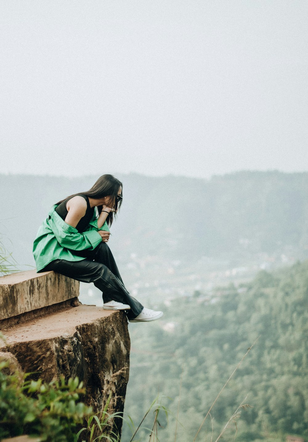 a person sitting on a ledge overlooking a forest