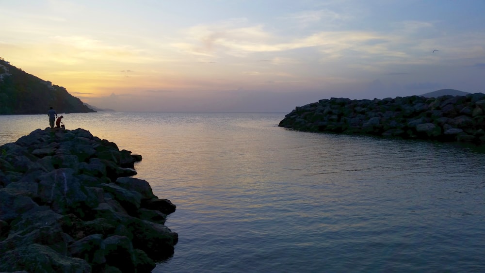 a rocky shore with a body of water and a couple people on it