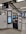 A modern ticket vending machine is situated in a clean subway station. There are clear signage and escalators leading to an exit marked 'Rodney Street'. The machine features a touchscreen interface displaying a map and options for purchasing tickets.
