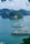 Cruise ships are sailing on tranquil blue-green waters, surrounded by lush green limestone islands. The expansive scene is framed by a bright, cloudy sky and leafy branches in the foreground, creating a peaceful and picturesque maritime landscape.