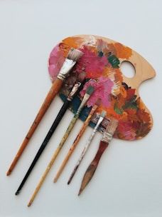 A colorful array of paintbrushes and palettes arranged on a wooden table.