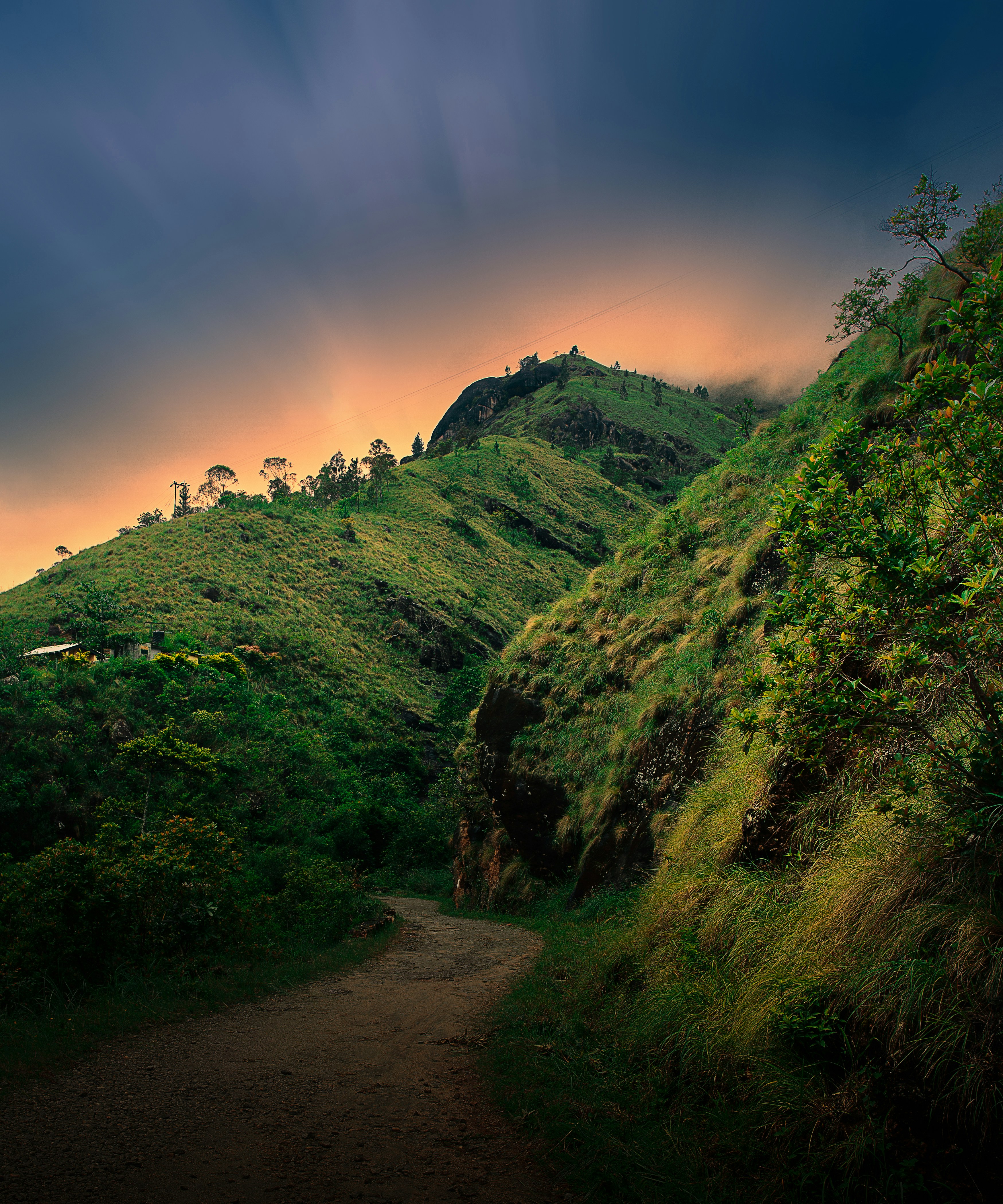 a dirt road leading up to a hill with trees and a sunset