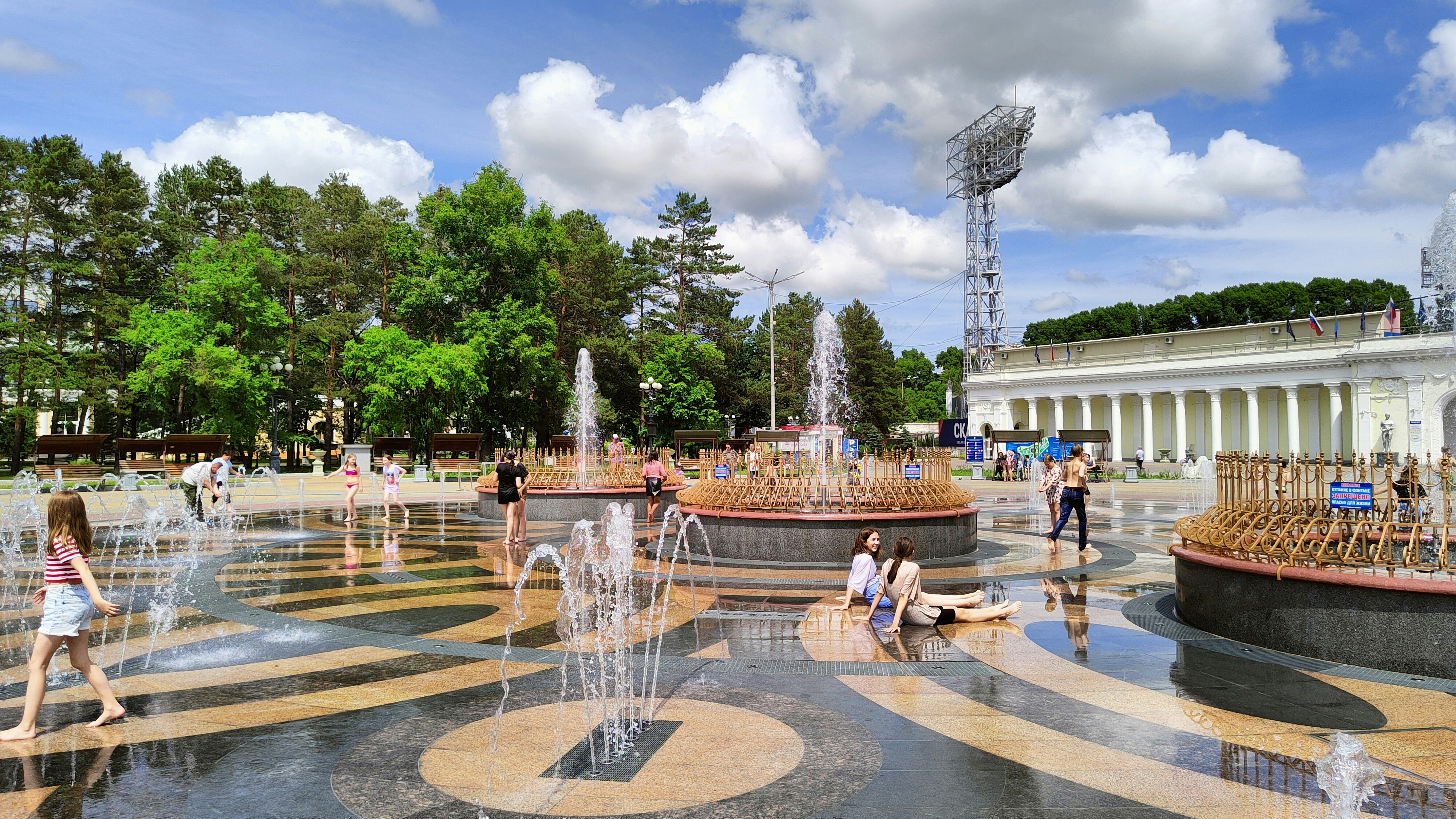 a group of people standing around a fountain in a courtyard with trees and a building in the background