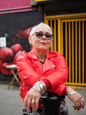 An older woman with silver hair rocking a leather jacket and bold sunglasses on a city street.