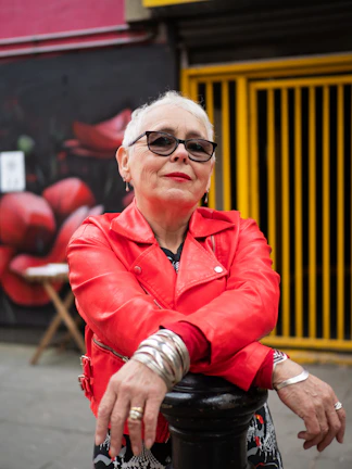 An older woman with silver hair rocking a leather jacket and bold sunglasses on a city street.