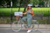 Smiling woman wearing a helmet, standing next to a green e-bike with Central Park trees in the background.