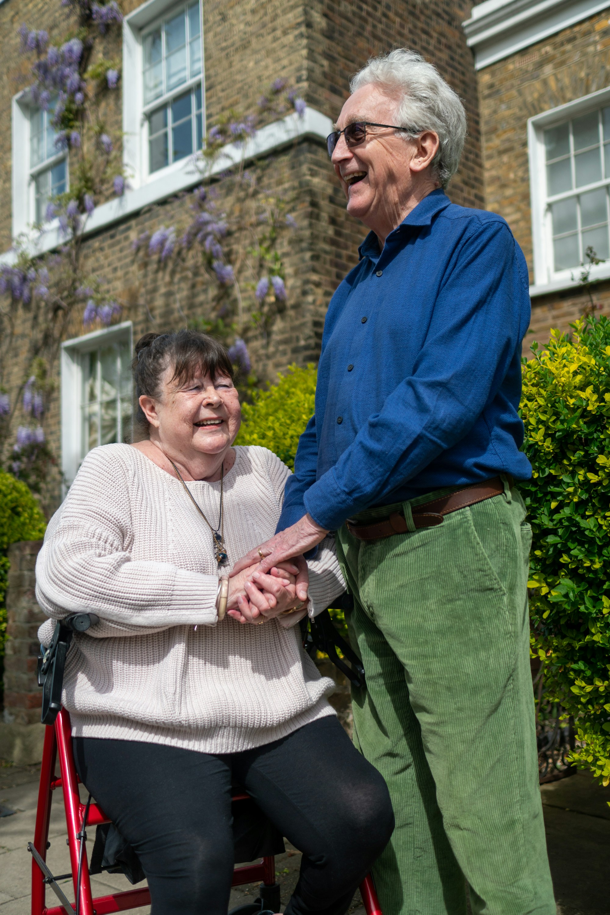An older couple with disabilities hold hands outdoors.