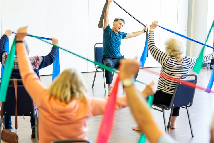 An older adult doing a supervised strength exercise with light dumbbells in a bright gym