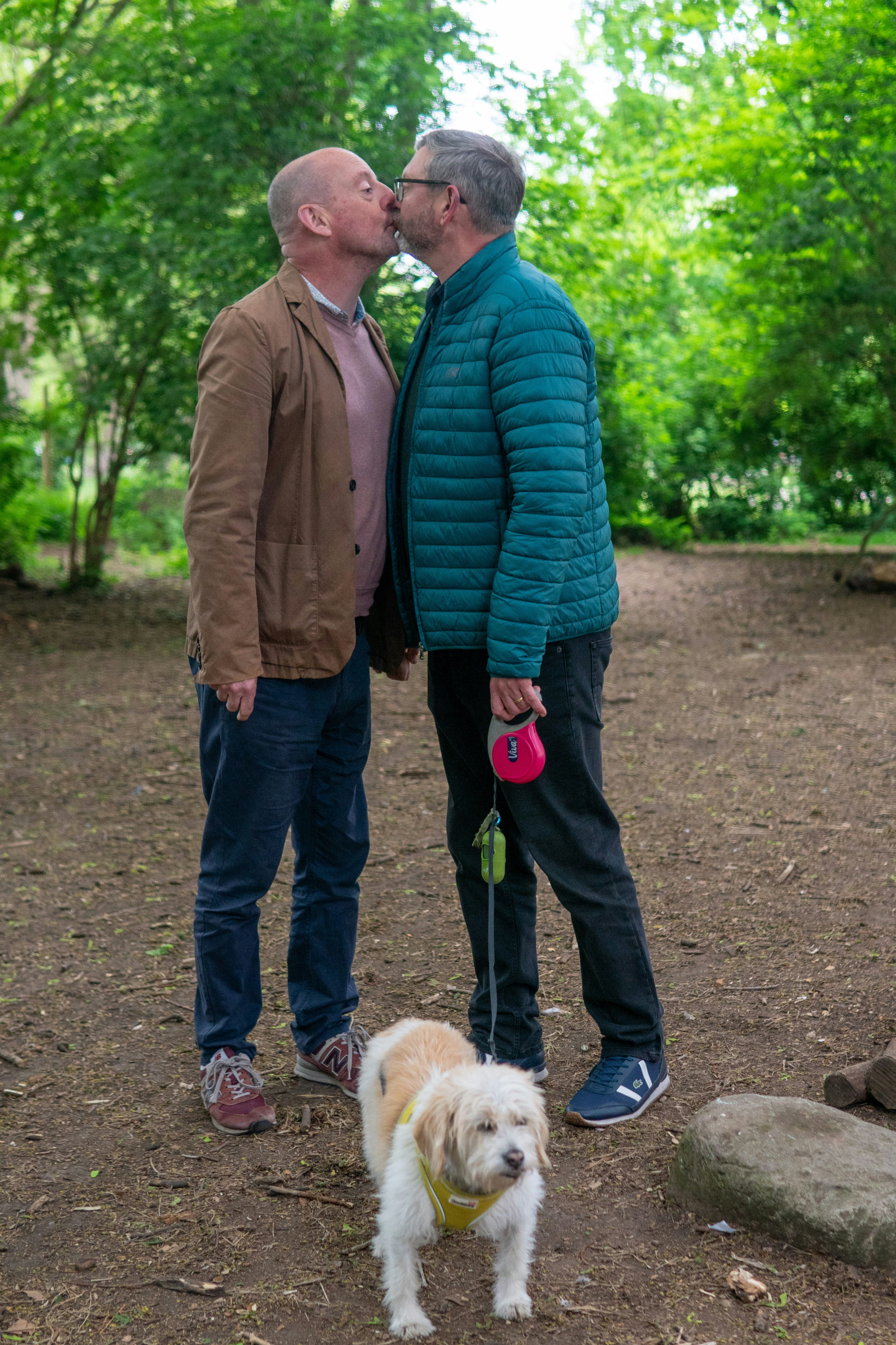 Gay couple kissing with their dog in the park.