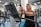 An elderly person is exercising on a stationary bike in a gym setting. The environment is filled with various gym equipment and modern fitness machines. The person appears focused and determined, wearing casual workout attire.