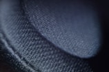 A close-up image focused on a textured surface that appears to be a fabric or textile. The surface is detailed, with visible fibers and a soft sheen, casting shadows that create a sense of depth.
