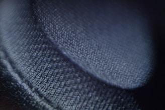 A close-up image focused on a textured surface that appears to be a fabric or textile. The surface is detailed, with visible fibers and a soft sheen, casting shadows that create a sense of depth.